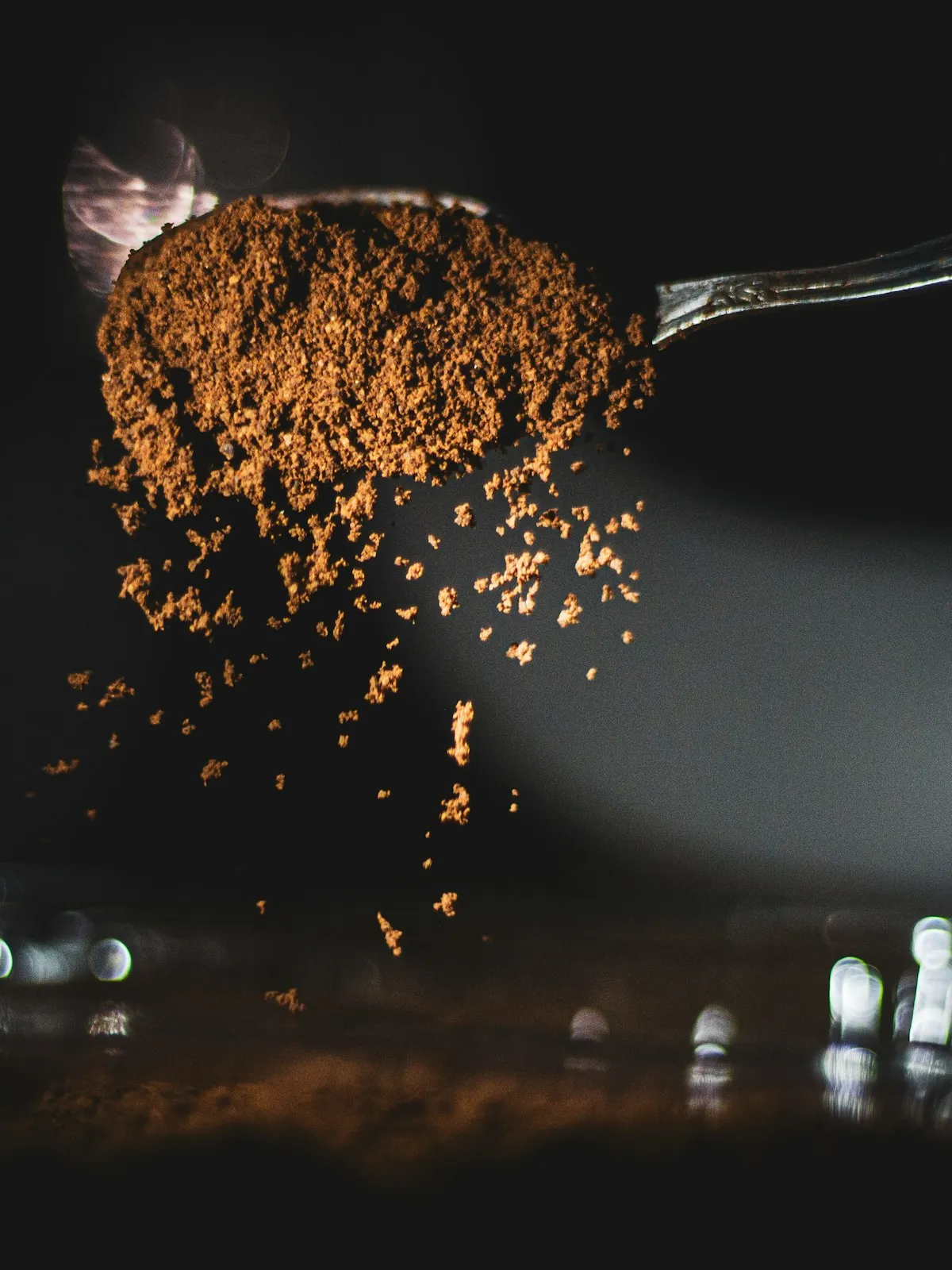 A spoonful of ground spice falling through a beam of light onto a dark surface
