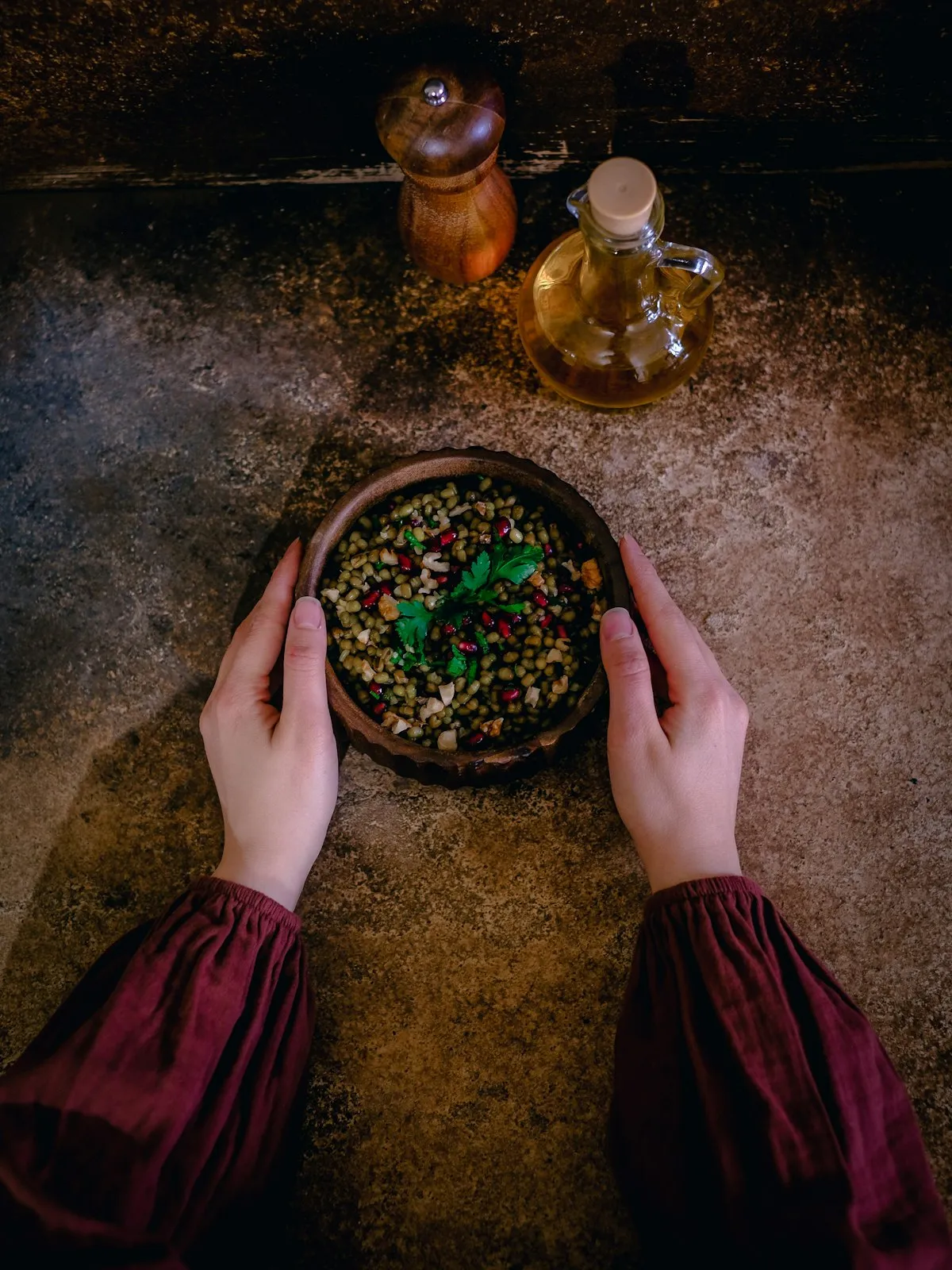 Hands holding a clay bowl of spiced lentils on a dark stone table