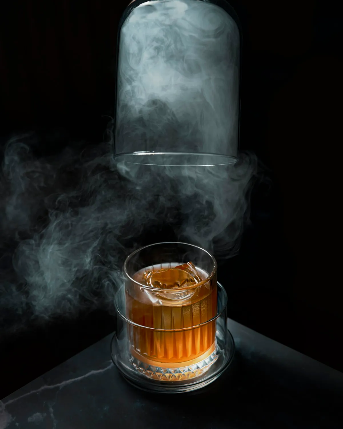 A smoked old fashioned, the smoke curling up from under a glass cloche