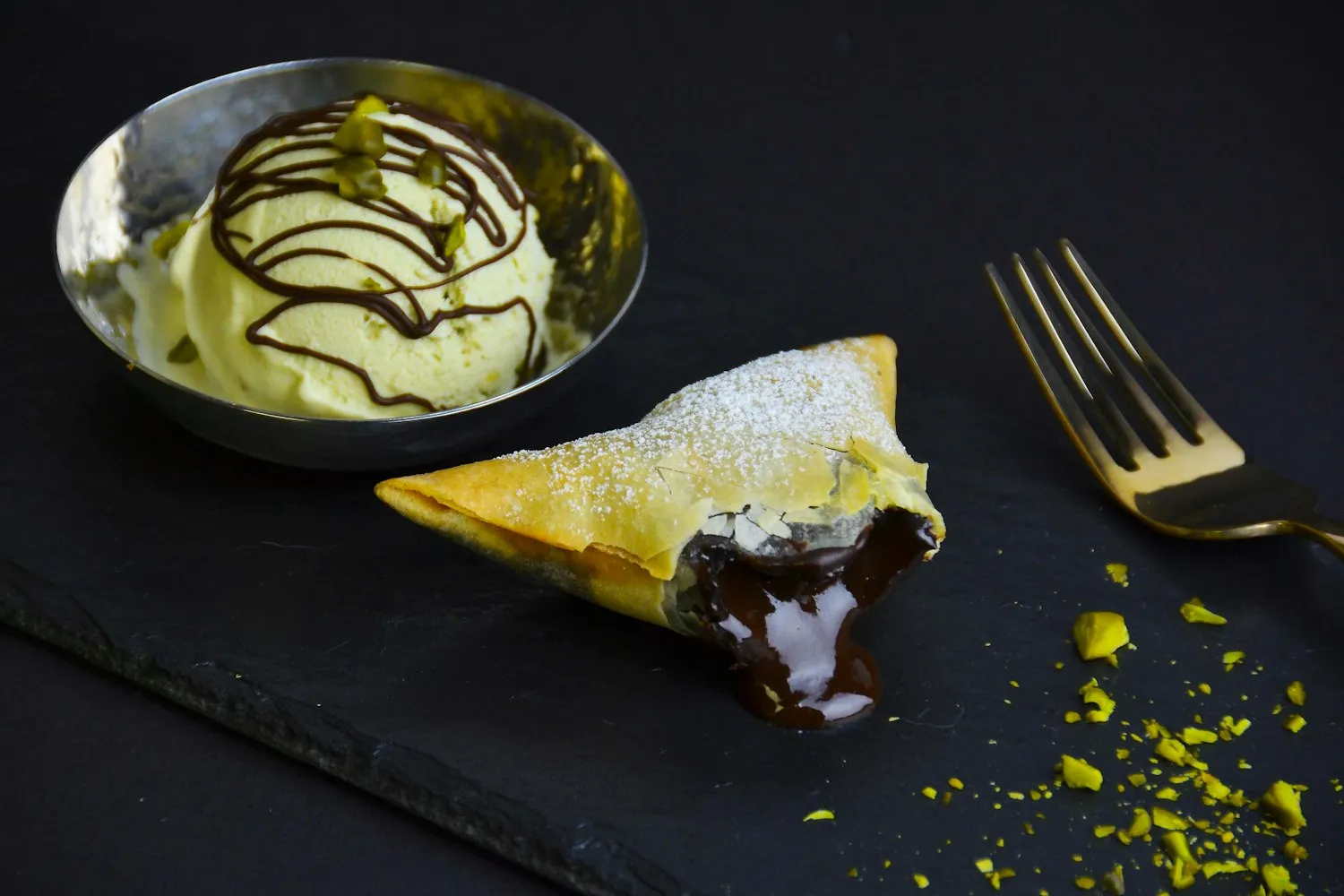 Pistachio ice cream beside a chocolate-filled pastry on dark slate