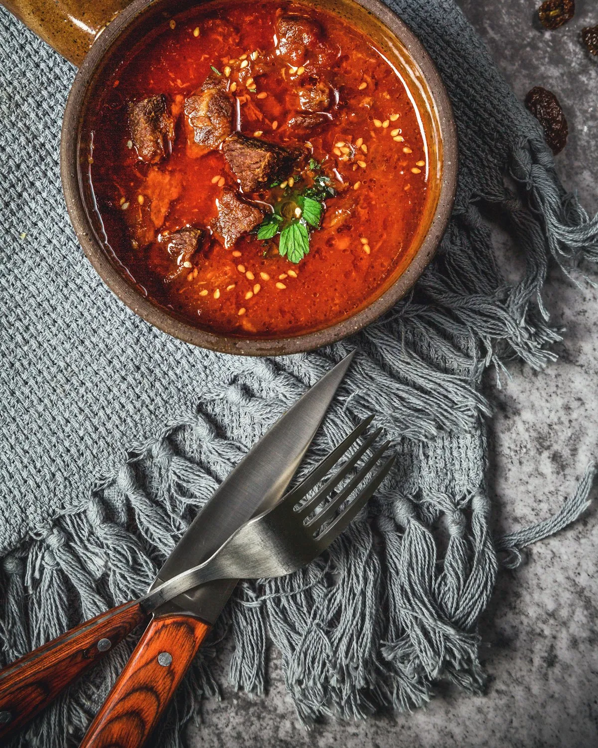 A deep red lamb curry in a clay bowl, seen from above